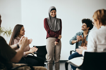 Happy Muslim woman receives applause from participants of group therapy after talking about her...