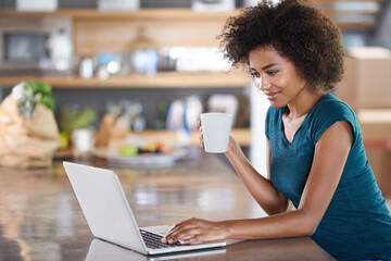 Having coffee with a friend. Young woman using a laptop while drinking from a mug.