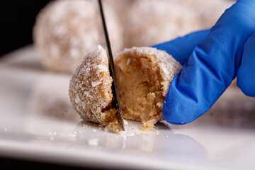 Beautiful sweets with coconut are cut with a knife on a white plate on a black background