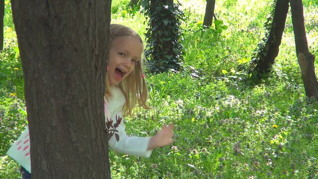 Kid Playing Hide and Seek in Forest, Child Hiding behind Tree, Happy Smiling Girl Plays in Spring Flowers, Children in Nature