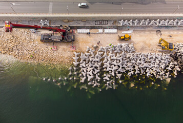 Aerial view of breakwater construction. Bulldozer and crane on a pile of boulders in the sea - obrazy, fototapety, plakaty