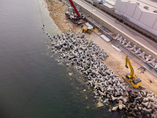 Aerial view of breakwater construction. Bulldozer and crane on a pile of boulders in the sea