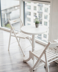 Beautiful white interior: table, two wooden chairs, panoramic windows, city view, potted plant