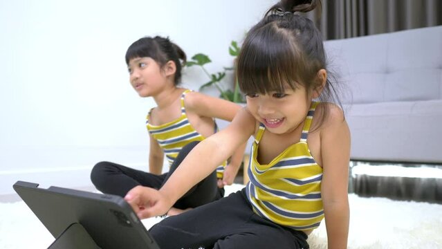 Sibling asian girl sitting and preparing to meditation pose, training on tablet in living room, smile with happy