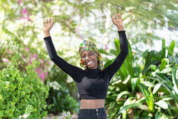 Gorgeous African girl in pants and long-sleeved black crop top standing in a flourishing garden...