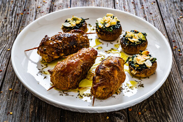 Wrapped pork meat with white mushrooms stuffed spinach almonds and mozzarella cheese on wooden table
