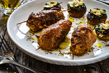 Wrapped pork meat with white mushrooms stuffed spinach almonds and mozzarella cheese on wooden table
