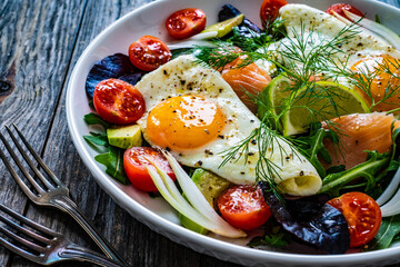 Salmon salad - smoked salmon, sunny side eggs,  avocado and fresh vegetables on wooden table
