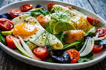 Salmon salad - smoked salmon, sunny side eggs,  avocado and fresh vegetables on wooden table
