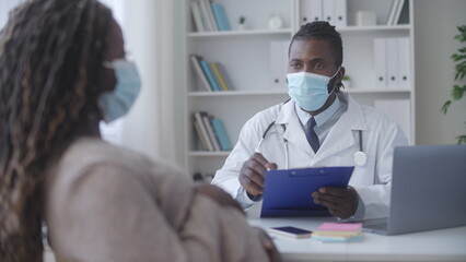 Black pregnant female telling complaints to obstetrician in face mask, check-up