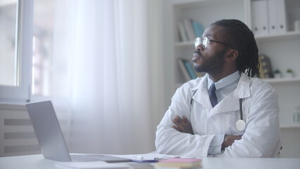 African American doctor sitting in his office and looking at window, thinking about treatment strategy