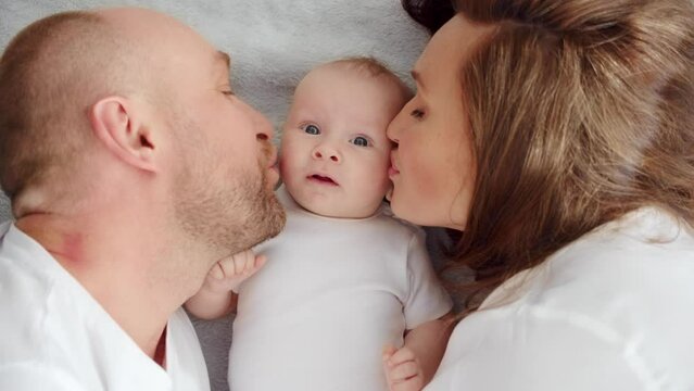 Happy parents kissing his newborn baby with, top view. Happy family.  Healthy newborn baby with mom and dad. Close up Faces of the mother, father and infant baby.  Cute  Infant boy and parents.