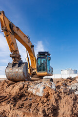 Obraz premium A powerful caterpillar excavator digs the ground against the blue sky. Earthworks with heavy equipment at the construction site.