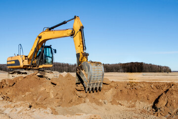 Fototapeta na wymiar A powerful caterpillar excavator digs the ground against the blue sky. Earthworks with heavy equipment at the construction site.