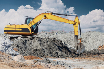 A powerful excavator digs the ground against the blue sky. Earthworks with heavy equipment at the...