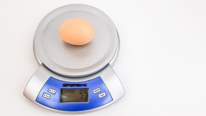 a large chicken egg is weighed on a kitchen scale. the image is isolated on white. good bird