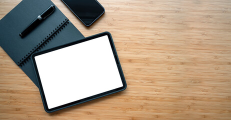 Top view of blank white screen digital tablet, notebook, pen and mobile phone on wooden table, copy space