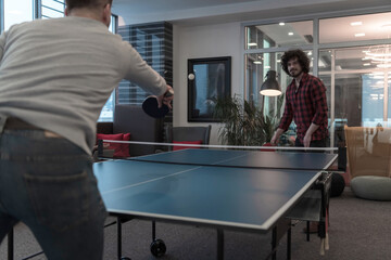 Two young start up business man playing ping pong tennis at modern creative office space people...