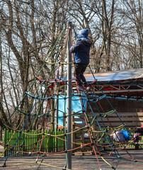A child is playing in the children's playground, climbing on some ropes, at a height. 