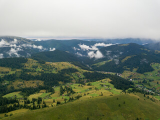 Obraz premium Green slopes of Ukrainian Carpathian mountains in summer. Cloudy morning, low clouds. Aerial drone view.