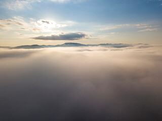 Flight over fog in Ukrainian Carpathians in summer. Mountains on the horizon. A thick layer of fog covers the mountains with a continuous carpet. Aerial drone view.