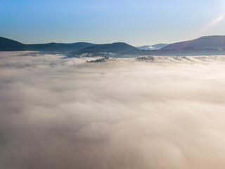 Flight over fog in Ukrainian Carpathians in summer. Mountains on the horizon. A thick layer of fog covers the mountains with a continuous carpet. Aerial drone view.
