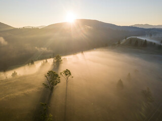 The rays of the morning sun through the fog in the mountains. Aerial drone view.