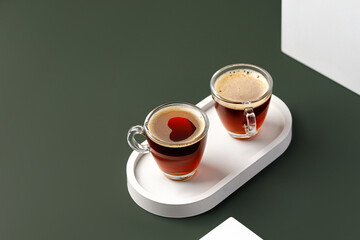 Two glasses coffee cup with espresso on beton tray and green background. Heart on foam, copy space