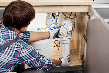 Plumber hand in gloves replace water filter cartridges at home kitchen. Fix purification osmosis system. Technician installing or repairing system of water filtration. - obrazy, fototapety, plakaty