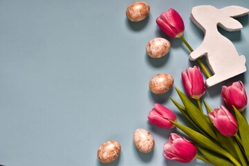 Easter composition. Pink bouquet tulips and easter eggs with decorative bunny on blue background. Flat lay. Top view with copy space. Happy easter greeting card