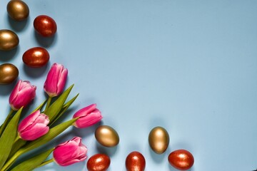 Obraz premium Easter composition. Pink bouquet tulips and easter eggs on blue background. Top view with copy space. Happy easter greeting card