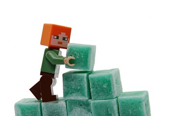 Naklejka premium LEGO Minecraft figure of Alex is building a wall from green coloured scented stearine wax cubes, white background