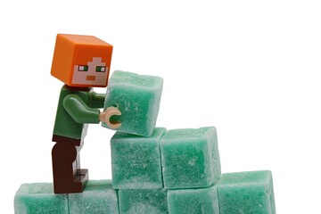 Obraz premium LEGO Minecraft figure of Alex is building a wall from green coloured scented stearine wax cubes, possibly of mint or eucalyptus scent, white background
