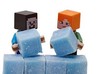 Obraz premium LEGO Minecraft figures of Steve and Alex building together a wall of light blue scented stearine wax cubes, white background