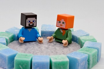Obraz premium LEGO Minecraft figures of Steve and Alex bathing in lavender scenty wax pool surrounded by green and blue coloured stearine wax cubes, light grey background.