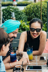 Group of Friends Using Digital Tablet Together in the Outdoor Cafe. 
Three happy friends watching something on a tablet while sitting in a restaurant and drinking coffee and cocktails.