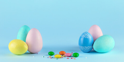 Colorful painted Easter eggs and sweet candy on blue background. Concept of happy Easter. Space for text.
