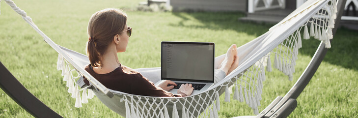 Young beautiful woman in hammock working on laptop computer panoramic banner. Freelance, working from home, enjoy life, student lifestyle, distance studying, travel, online learning concept