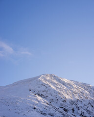 Fototapeta na wymiar Snow-covered mountain catching sunlight under a blue sky