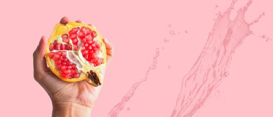 Hand squeezing, Pomegranate isolated on pink background and splashing fresh water with copy space,...