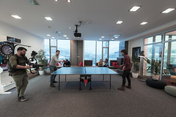 Man with camera recording two young business man playing ping pong tennis at modern creative office space people group have meeting and brainstorming in background