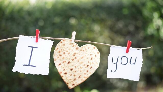 Notes with words "I", "you" and heart from  Matzah on blurry green background. Love is happiness and care. Couple's relationships and confessions of love.
