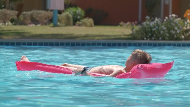 Young child boy relaxing on summer sun swimming on inflatable air mattress in swimming pool during tropical vacations. Summertime activities concept