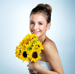 Fresh as flowers. Studio portrait of a beautiful young woman holding a bouquet of sunflowers.