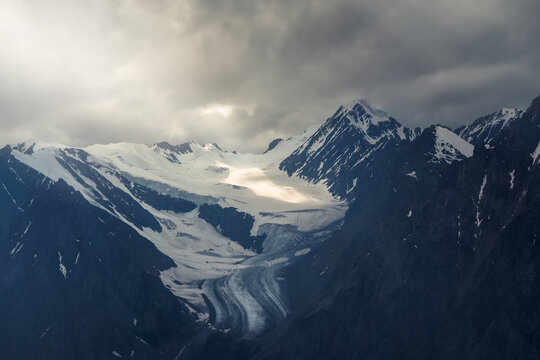 Mystical sunlight of heaven in the dark morning mountains. Dramatic sky on darkness mountain peaks. Mystical glacier background with dramatic mountains.
