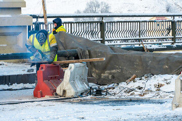 Employees of the road service in special yellow vests perform work on the repair of the roadway. Road repairs in difficult winter conditions during severe frost.