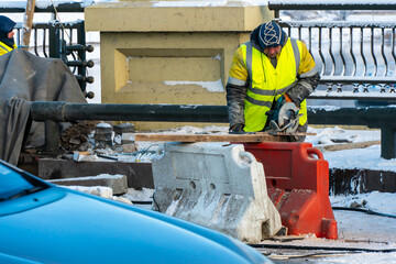 Fototapeta premium Employees of the road service in special yellow vests perform work on the repair of the roadway. Restoration of the deformation seam of the automobile bridge.