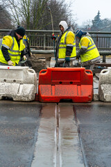 Fototapeta premium Employees of the road service in special yellow vests perform work on the repair of the roadway. Restoration of the deformation seam of the automobile bridge.