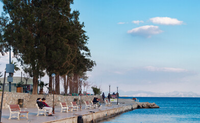 Fototapeta na wymiar Coastal area of Datça Peninsula in Turkey. People sitting on bench and watcing blue sea view. Quiet, peaceful seaside town. 