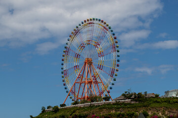 The huge ferris wheel or observation wheel on the hill on the background of blue cloudy sky.